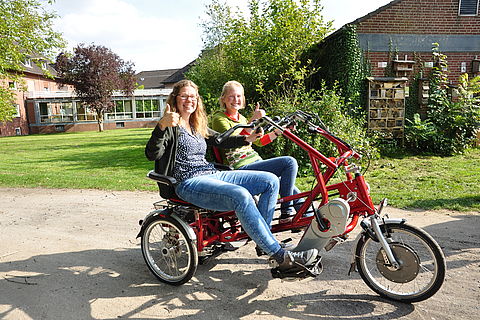Zwei junge Frauen fahren auf einen Dreirad-Tandem mit dem Namen Fun2Go.