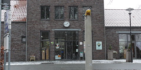 Vor dem Eingang zum Bahnhofscafé steht eine Säule mit der Skulptur eines Fantasietieres. Die Aufnahme ist im Winter gemacht. 